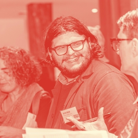 A person with a beard and glasses laughs while having a conversation. 