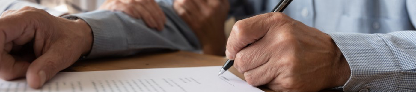 An elderly hand signing a form and another persons hand holds onto the arm of the elderly hand